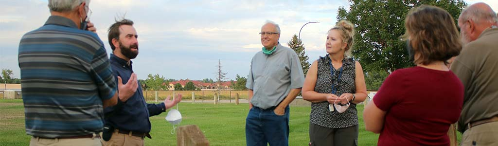 Group of adults in conversation outdoors, with trees and sky in the background.
