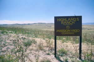 A sign for "Highlands Ranch" by Mission Viejo Company, set against a grassy landscape and clear blue sky.