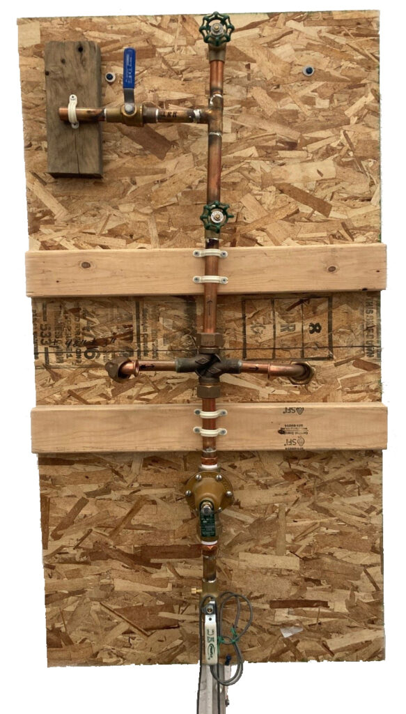 An array of copper pipes and valves mounted on a wooden board, possibly a plumber's training mock-up.