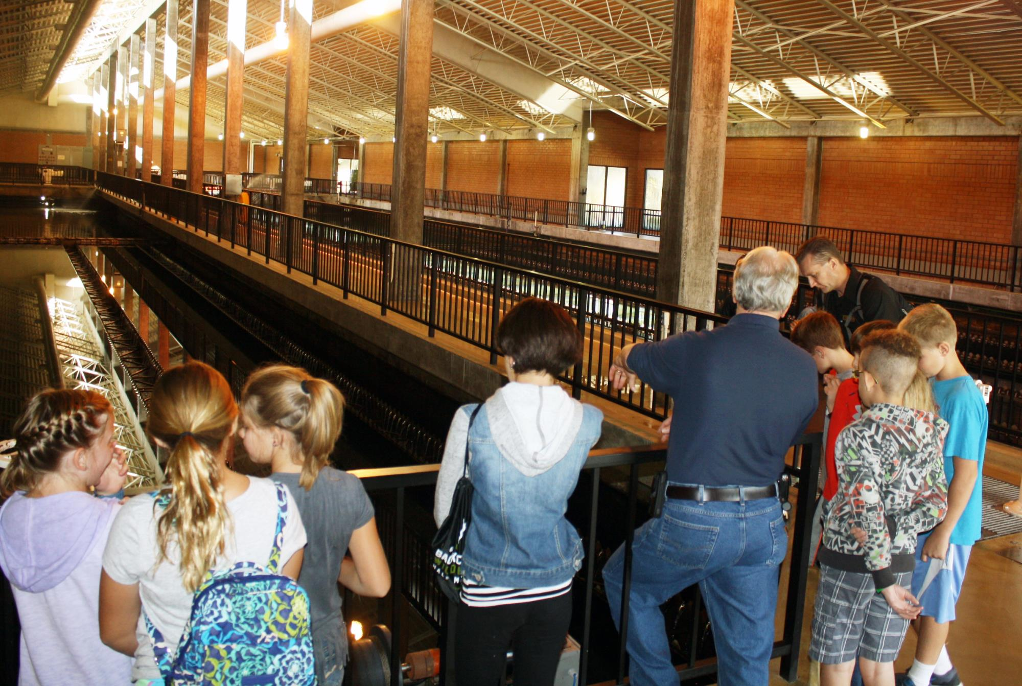 Group of people, most likely on a tour, observing machinery in an industrial-style building.