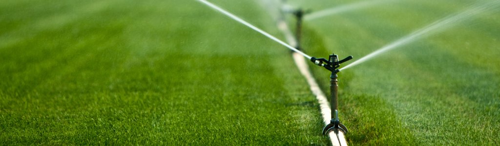 A lawn being irrigated with sprinklers, creating a bright green landscape filled with water droplets.