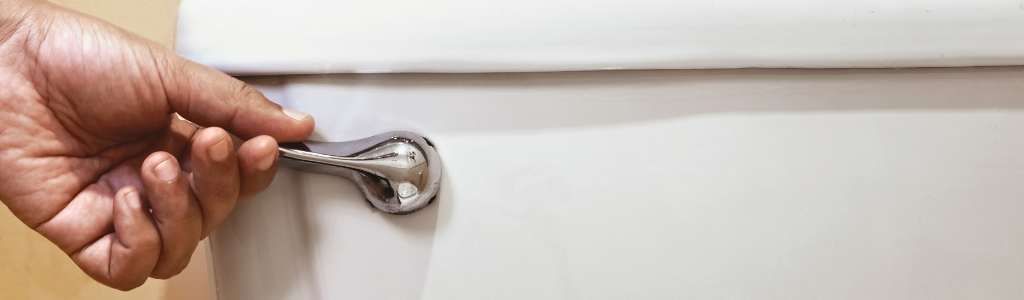 A hand is pulling the lever of a white toilet tank.
