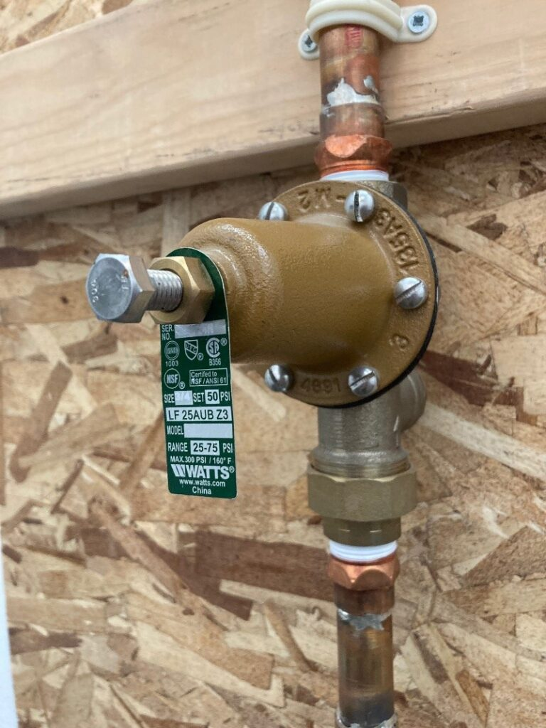A water pressure reducing valve with copper pipes on a wooden background.