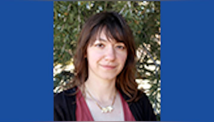 A woman with brown hair in front of greenery.