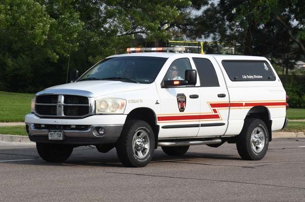 A white Dodge truck marked with red stripes, badges, and a "Life Safety Division" label on the side, parked on a road.
