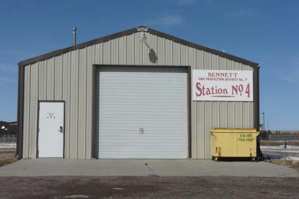 A small beige metal building labeled "Bennett Fire Protection District No. 7, Station No. 4" with a yellow dumpster outside.