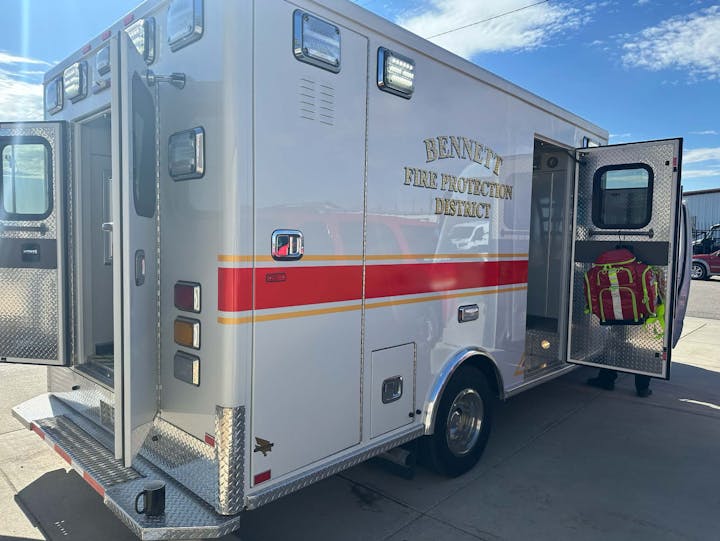 An ambulance with open doors, labeled "Bennett Fire Protection District," parked outdoors.
