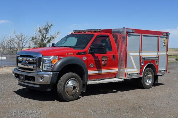 A red fire rescue truck with compartments, parked on a gravel surface.