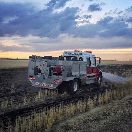 A fire truck spraying water on a charred field with a cloudy sky in the background.