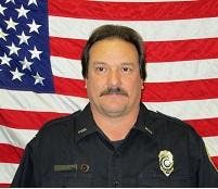 The image features a person in a police uniform standing in front of the American flag.