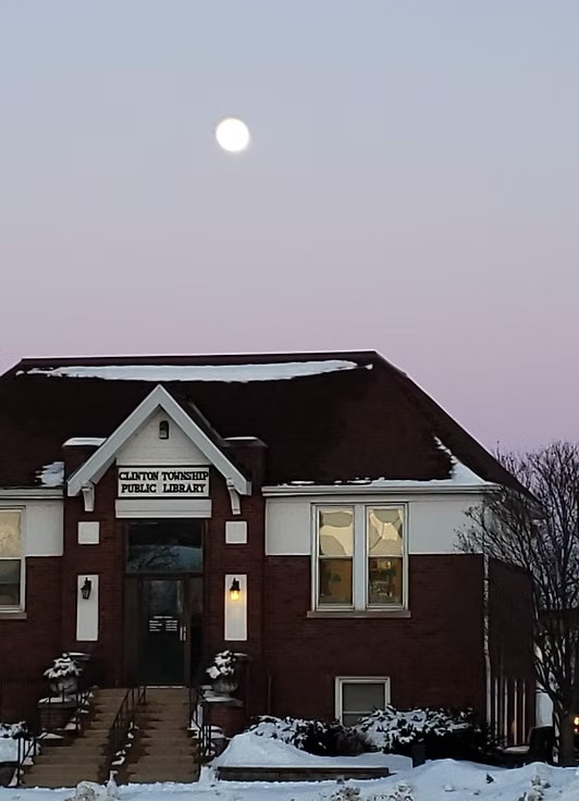 Brick public library building with snow-covered roof, under a moonlit sky.