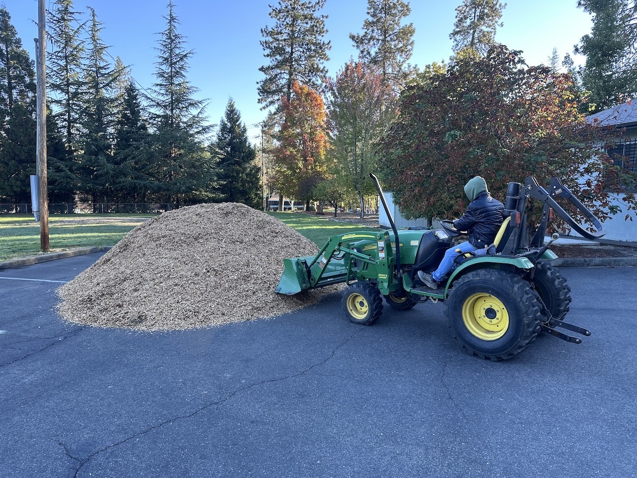 A large pile of mulch and a person on a green tractor, possibly preparing for landscaping work.