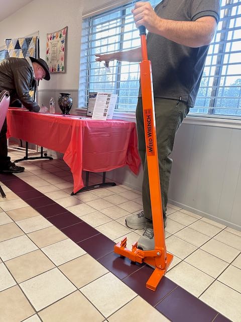 A person is using a manual pallet jack indoors, near a table with a red tablecloth and documents.