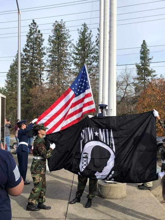 Members of a military honor guard display the American flag and a POW-MIA flag during a ceremonial event outdoors.