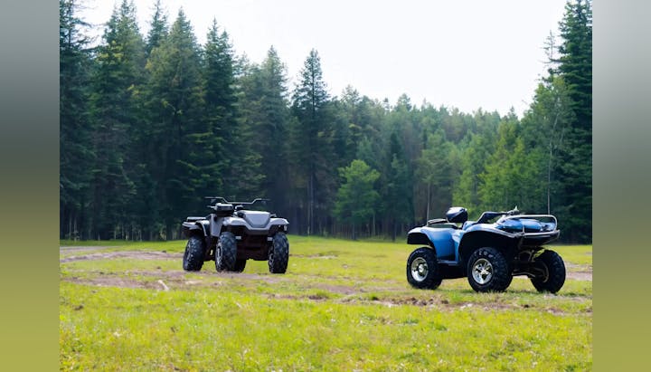 Two ATVs parked on grass with a forest backdrop.