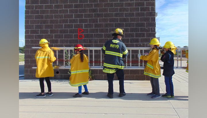 A firefighter and children in protective gear observing a building.