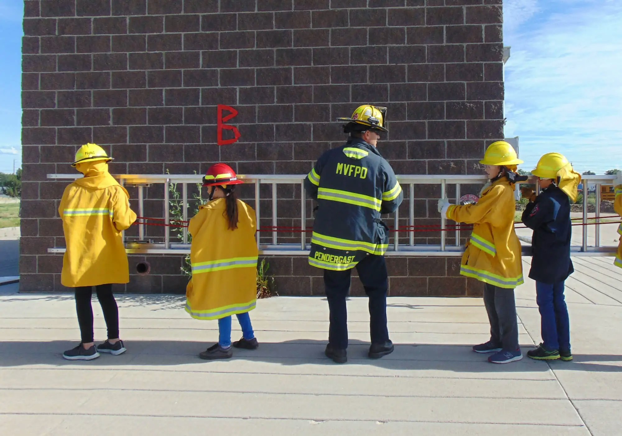 A firefighter and children in protective gear observing a building.