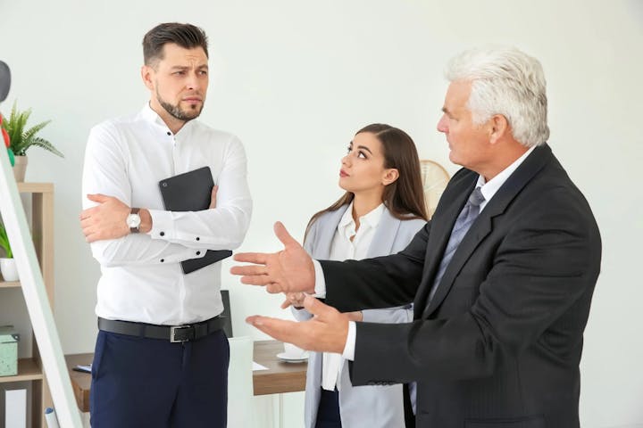Three professionals in a discussion, possibly a disagreement, in an office setting.