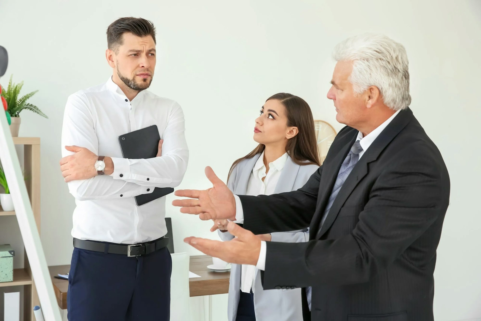 Three professionals in a discussion, possibly a disagreement, in an office setting.