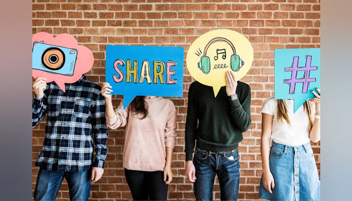 Four people holding up colorful social media icon signs against a brick wall.
