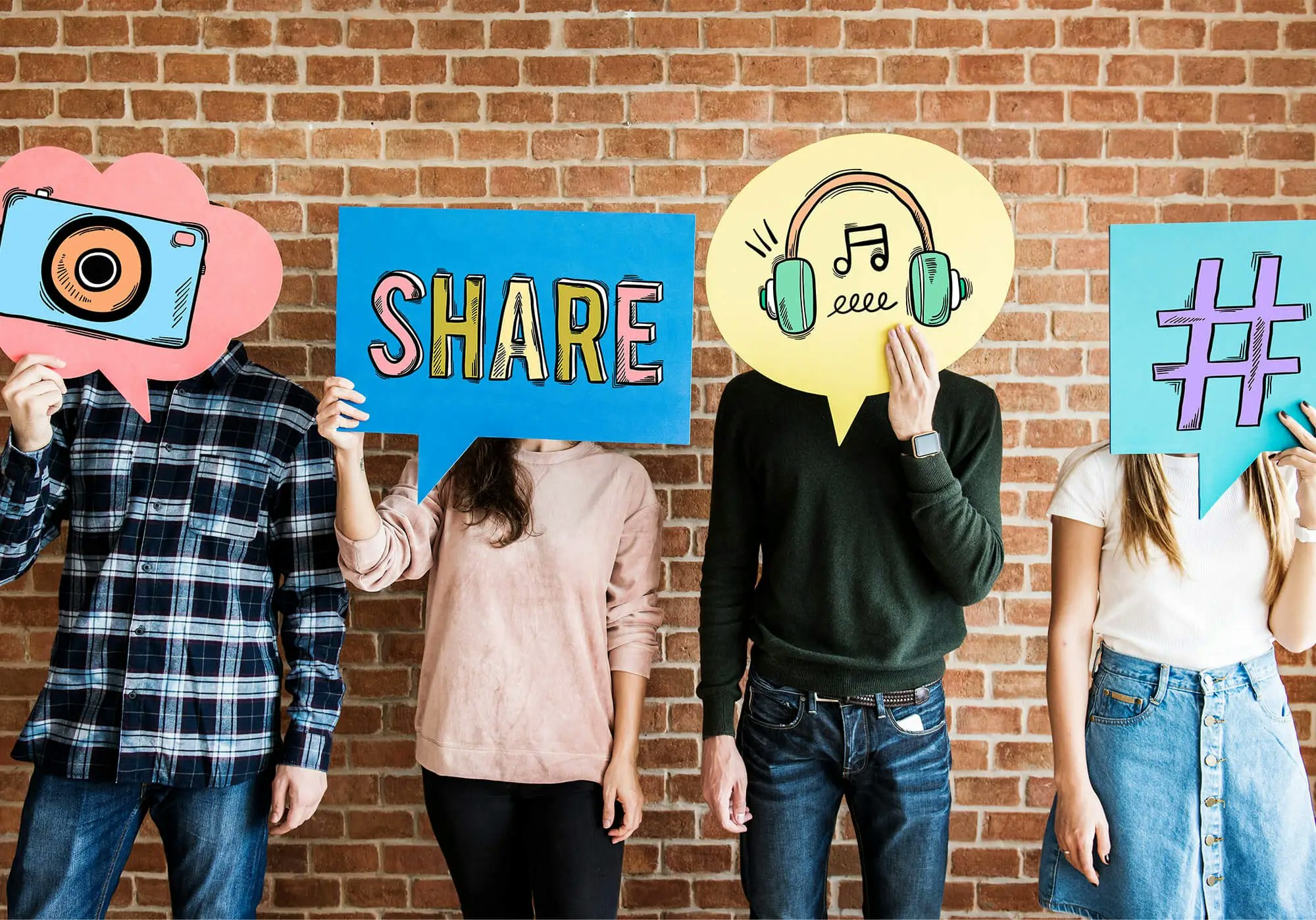 Four people holding up colorful social media icon signs against a brick wall.