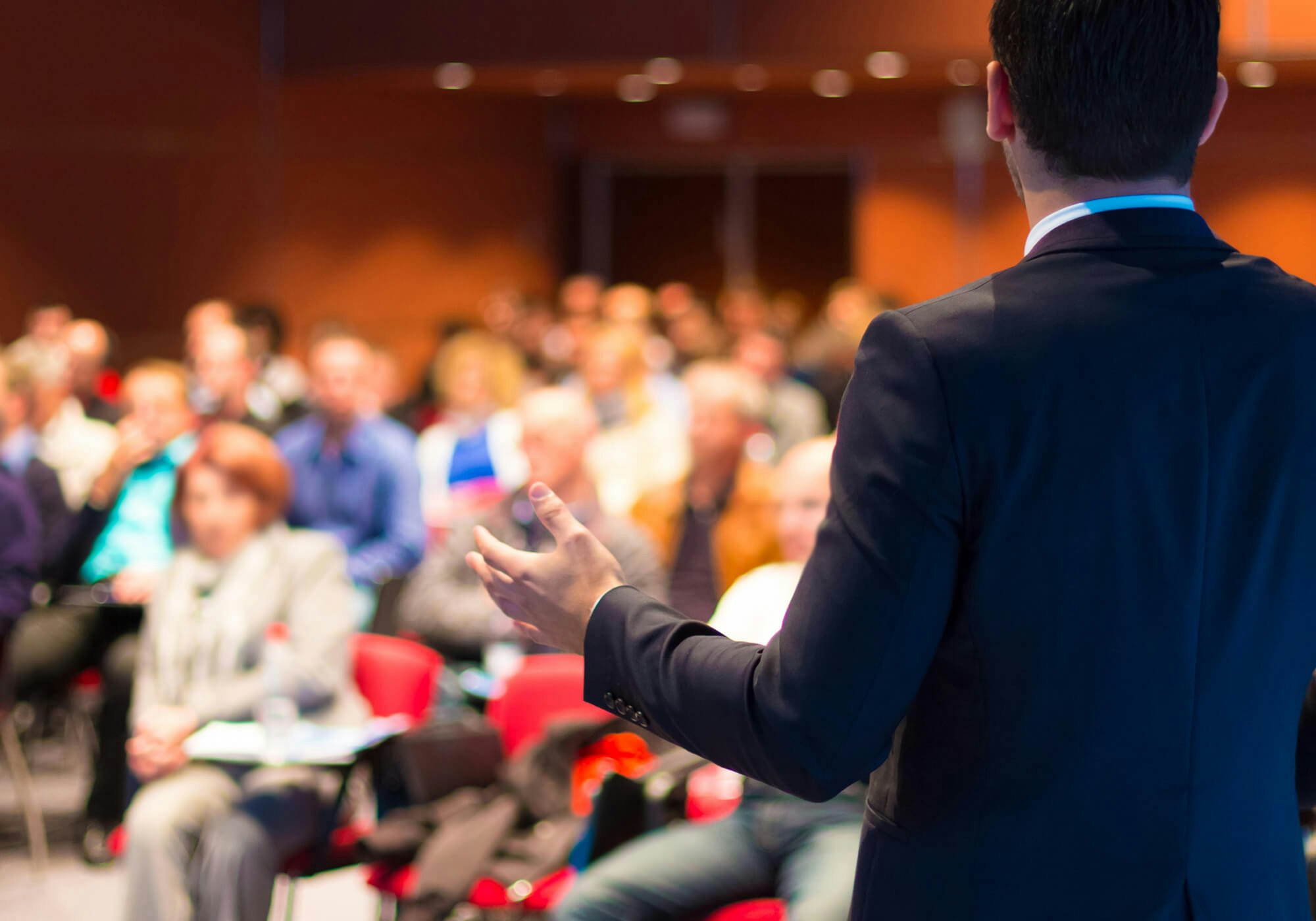 A speaker presenting to an audience in a conference room.