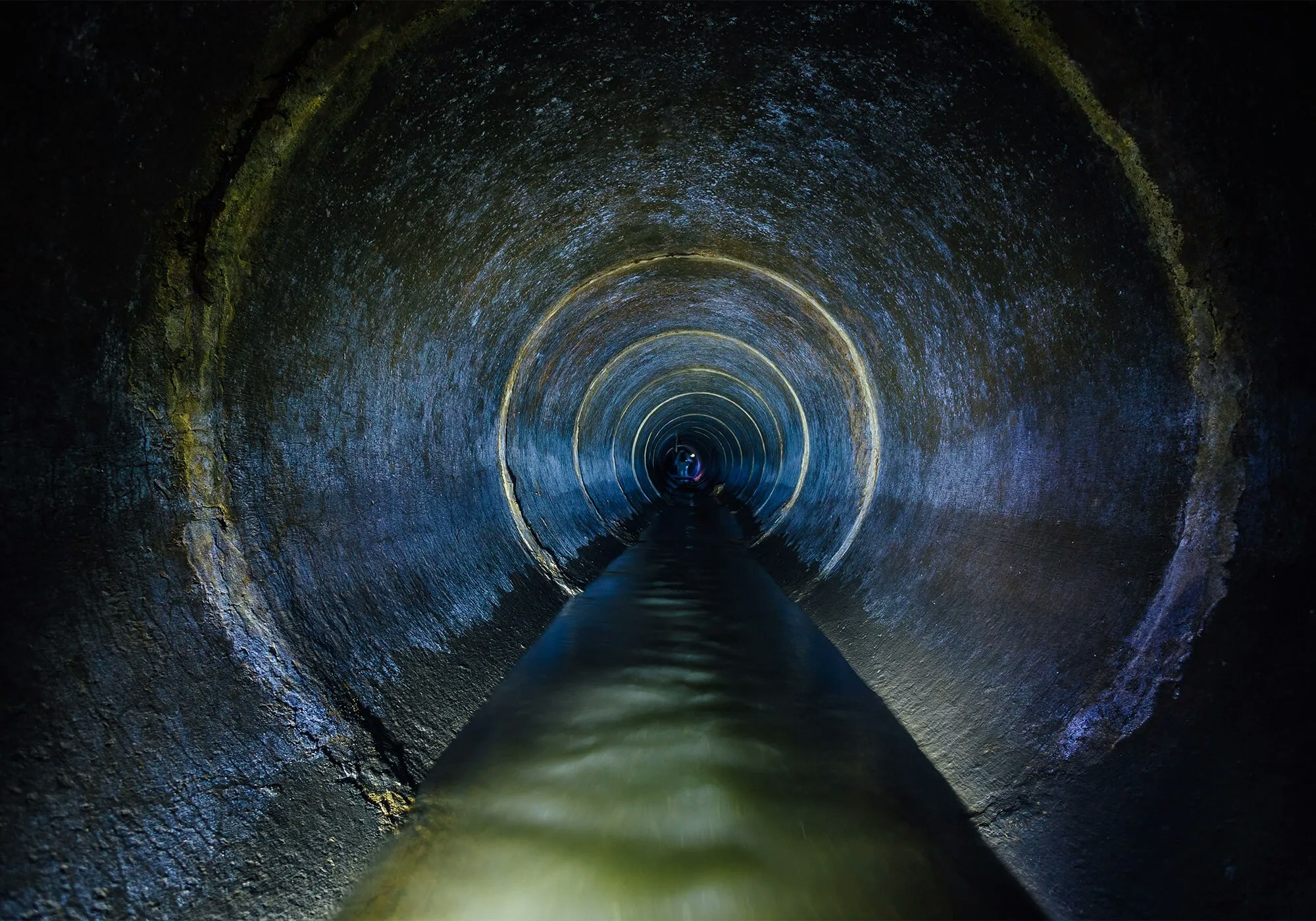 A dimly lit tunnel with water at the bottom, creating a circular reflection.