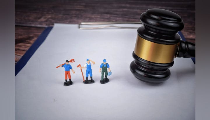 Miniature figures with tools next to a large gavel on paper.