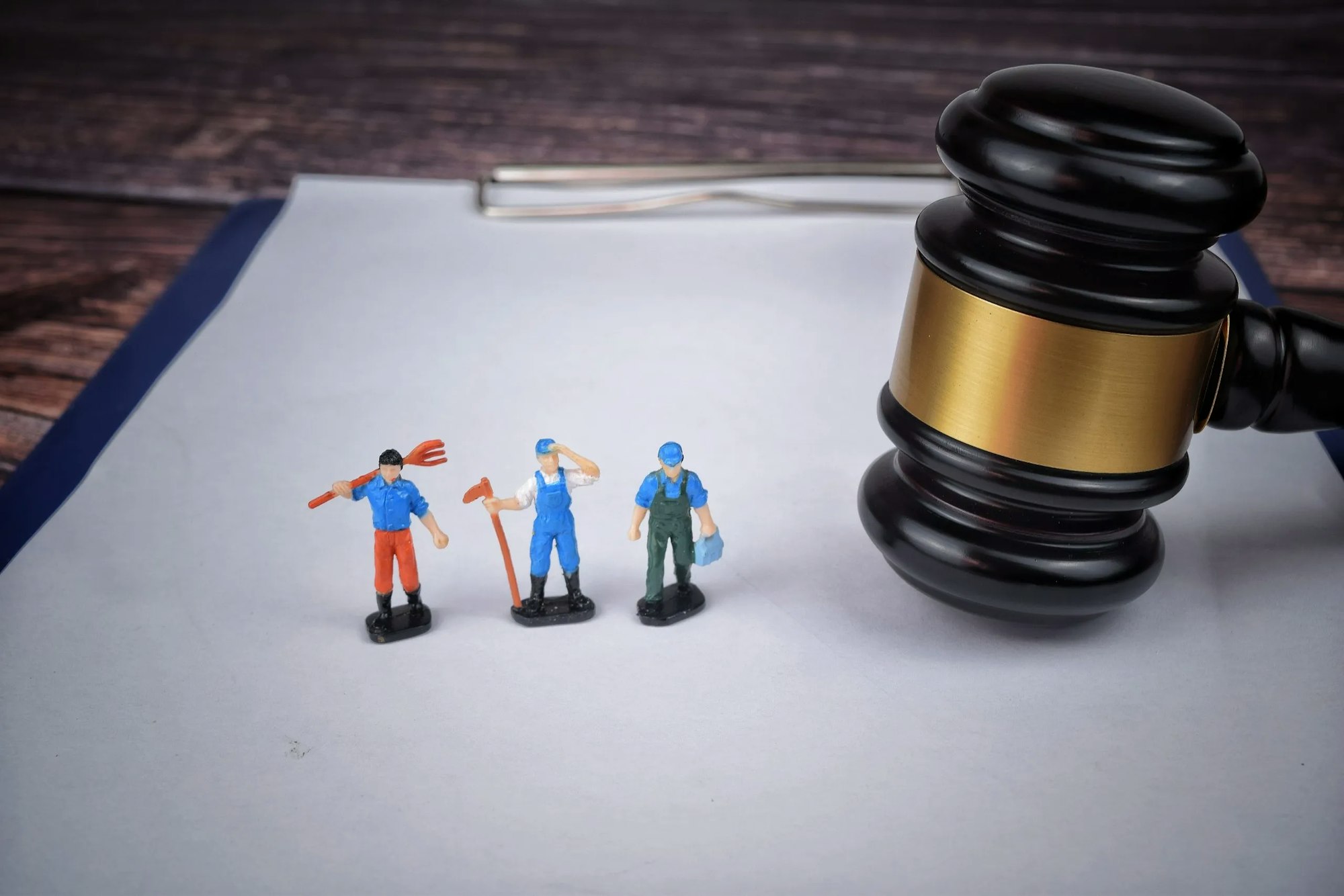 Miniature figures with tools next to a large gavel on paper.