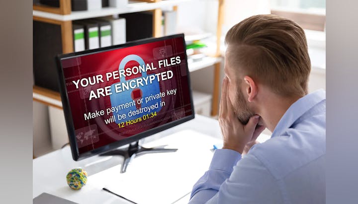 Man stressed by a ransomware message on his computer screen demanding payment to decrypt files.