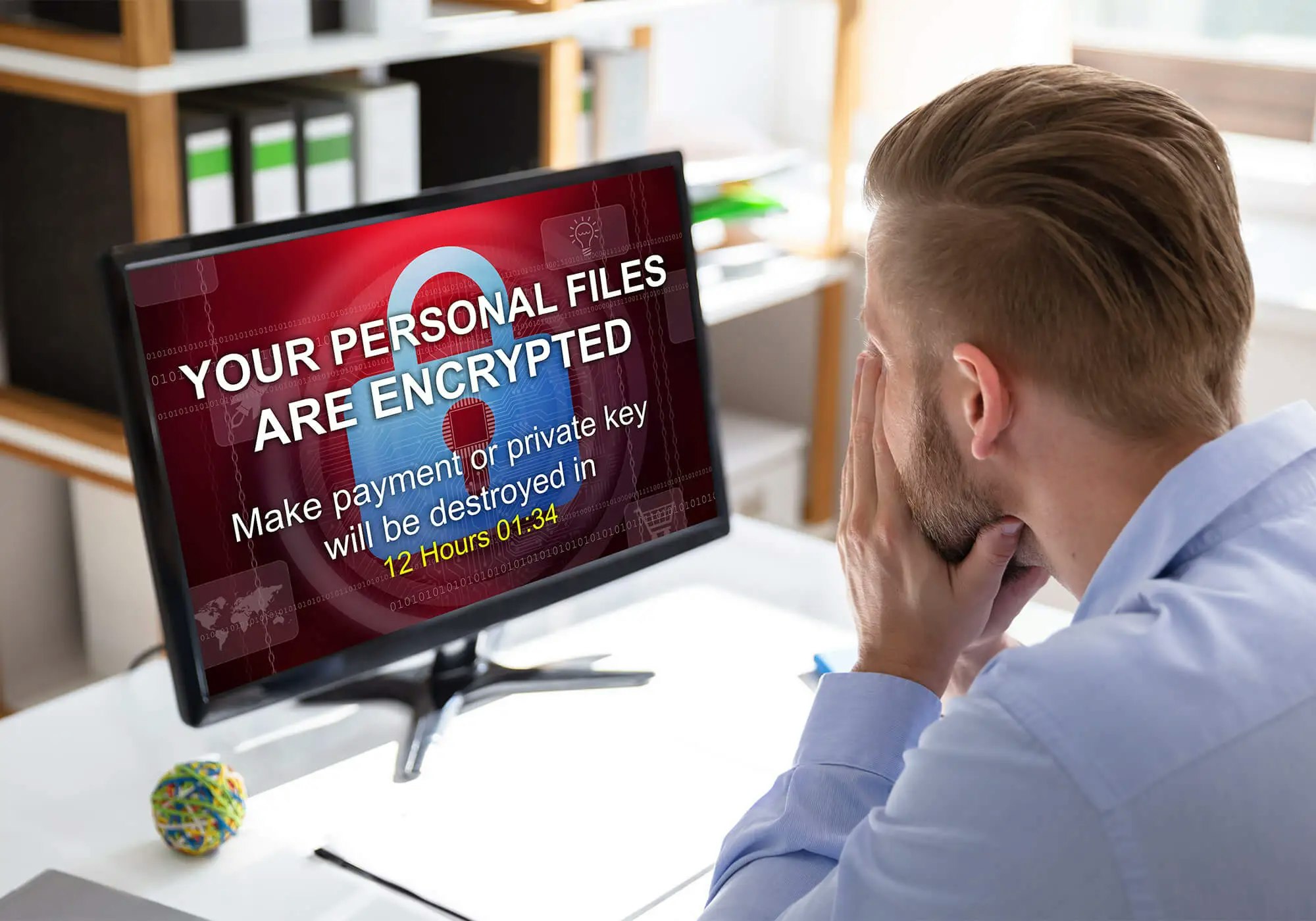 Man stressed by a ransomware message on his computer screen demanding payment to decrypt files.