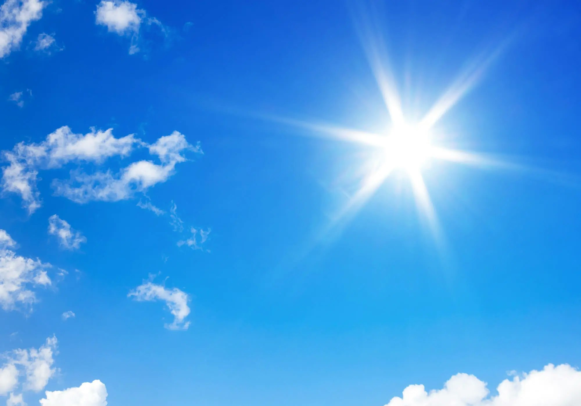 Bright sun with rays and blue sky with scattered clouds.