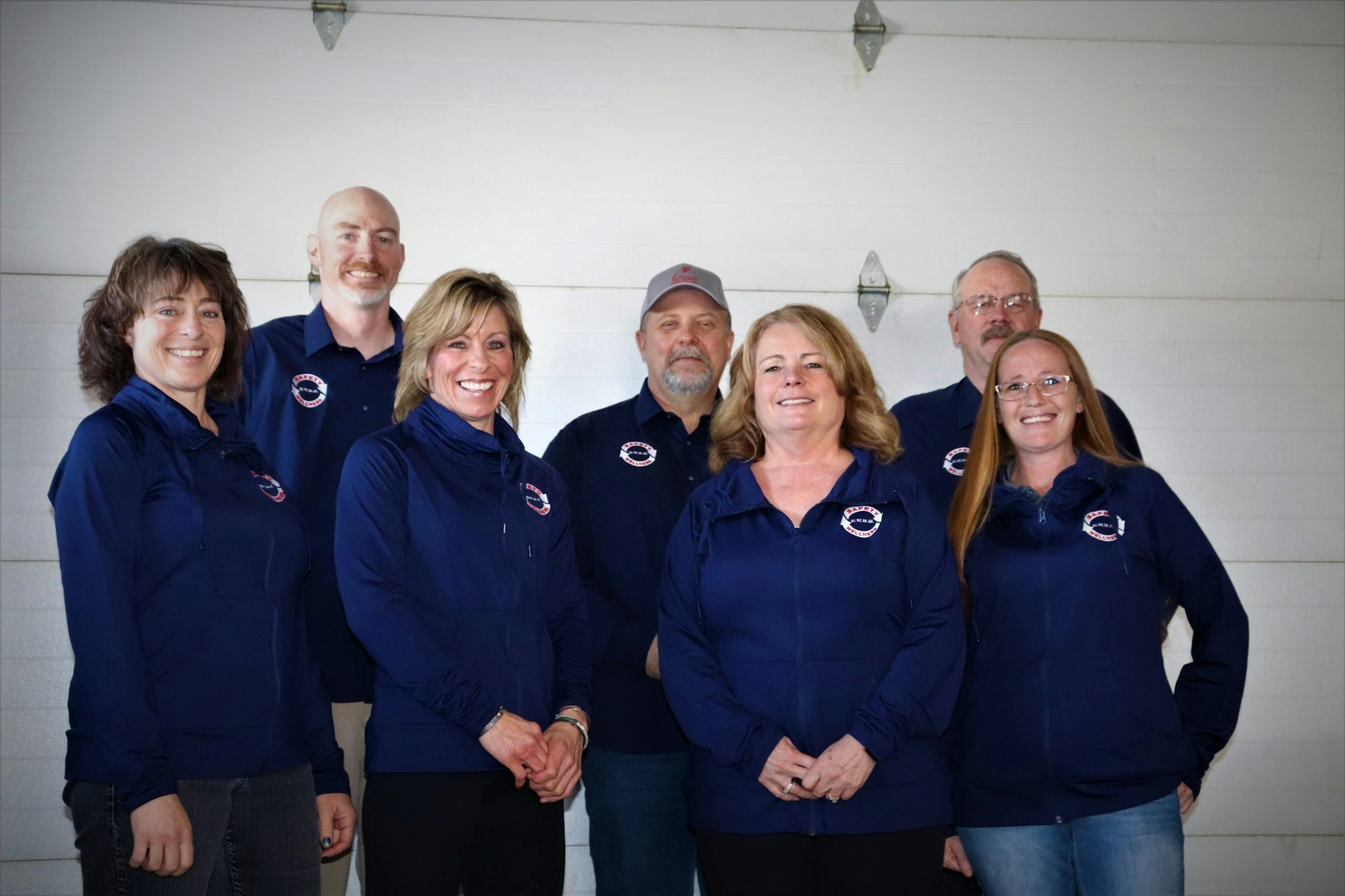 Group of people in matching blue jackets with logos, smiling indoors.