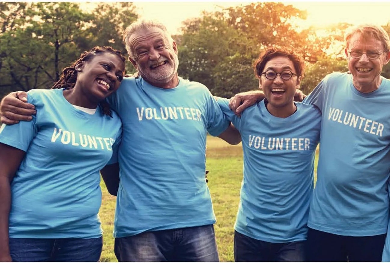 Four happy people wearing "VOLUNTEER" t-shirts outdoors.