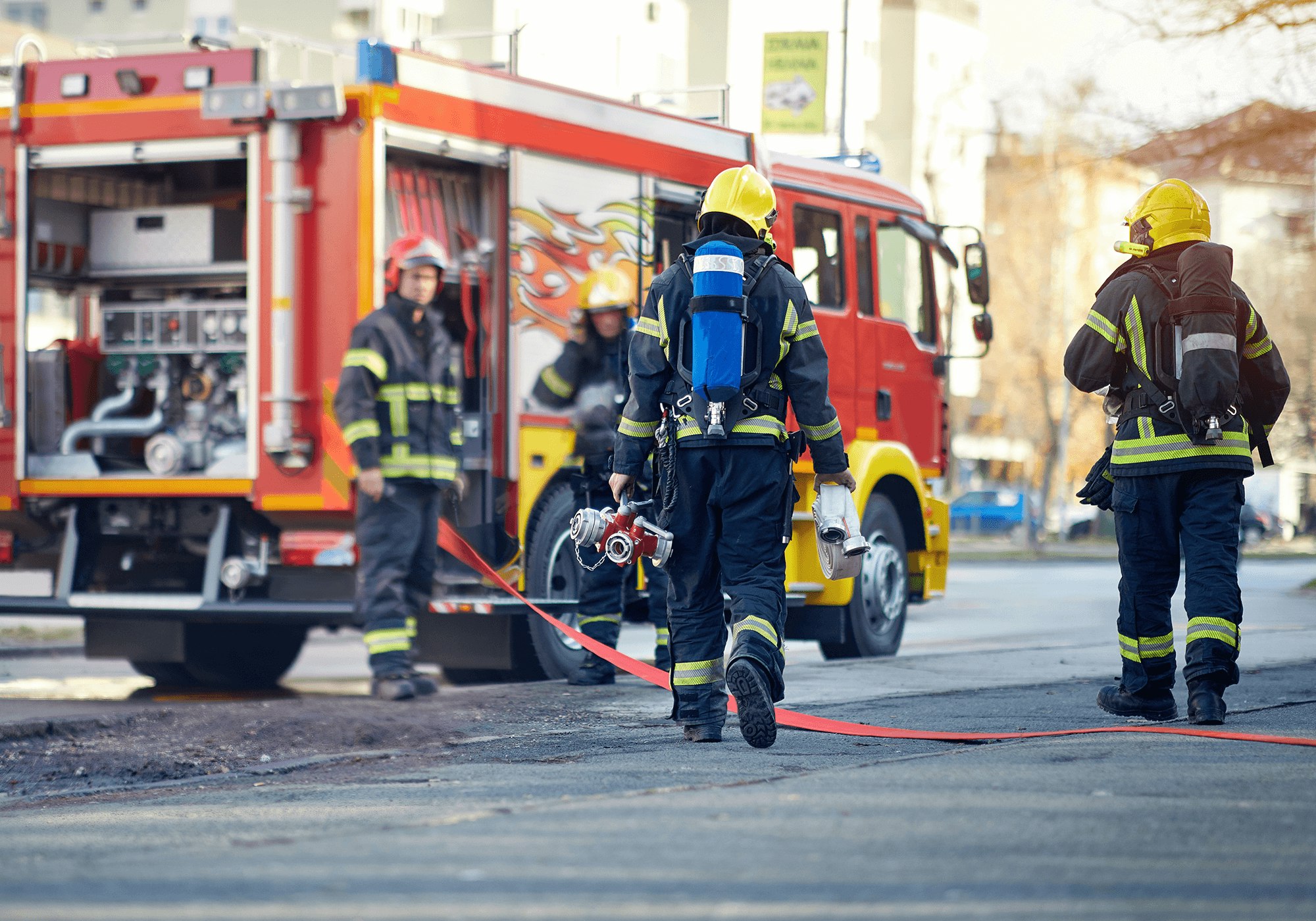 Firefighters in gear approaching an emergency with a fire truck in the background.