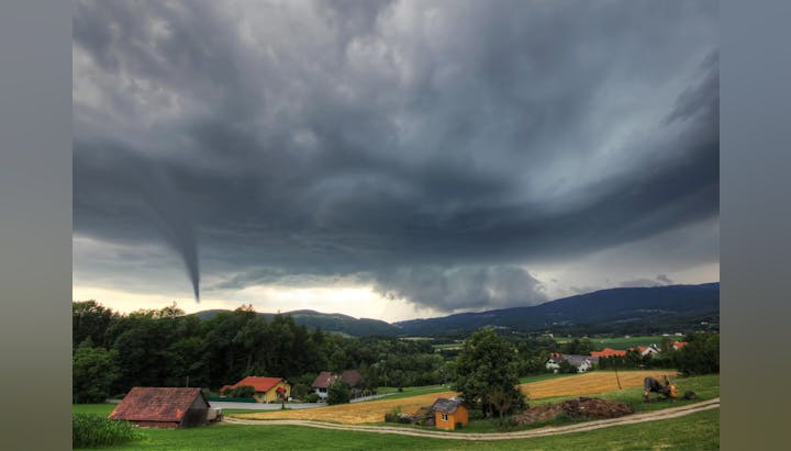 A tornado forming above a rural landscape under dark stormy skies.