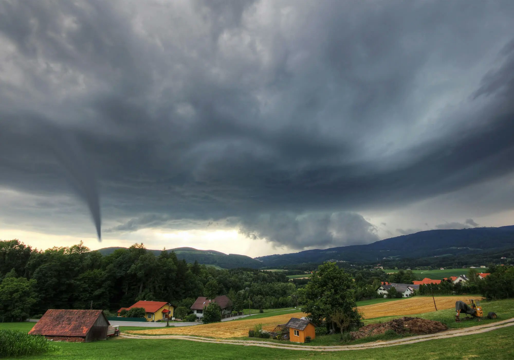 A tornado forming above a rural landscape under dark stormy skies.
