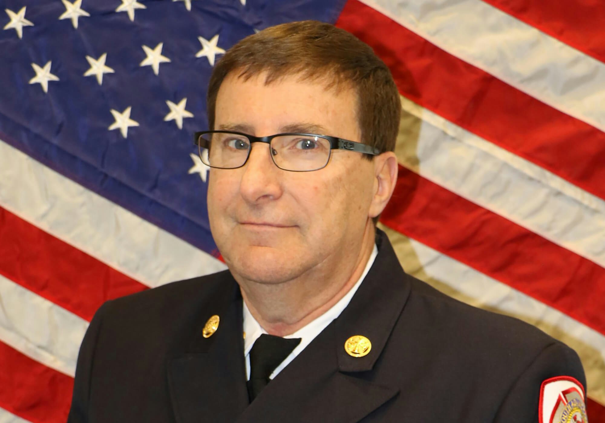 A person in uniform with insignia in front of an American flag.