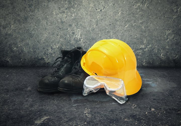 Safety gear with helmet, boots, and goggles on a rough surface.