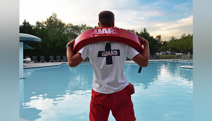 Lifeguard standing by a pool with a rescue buoy, ready to ensure swimmer safety during a tranquil evening.