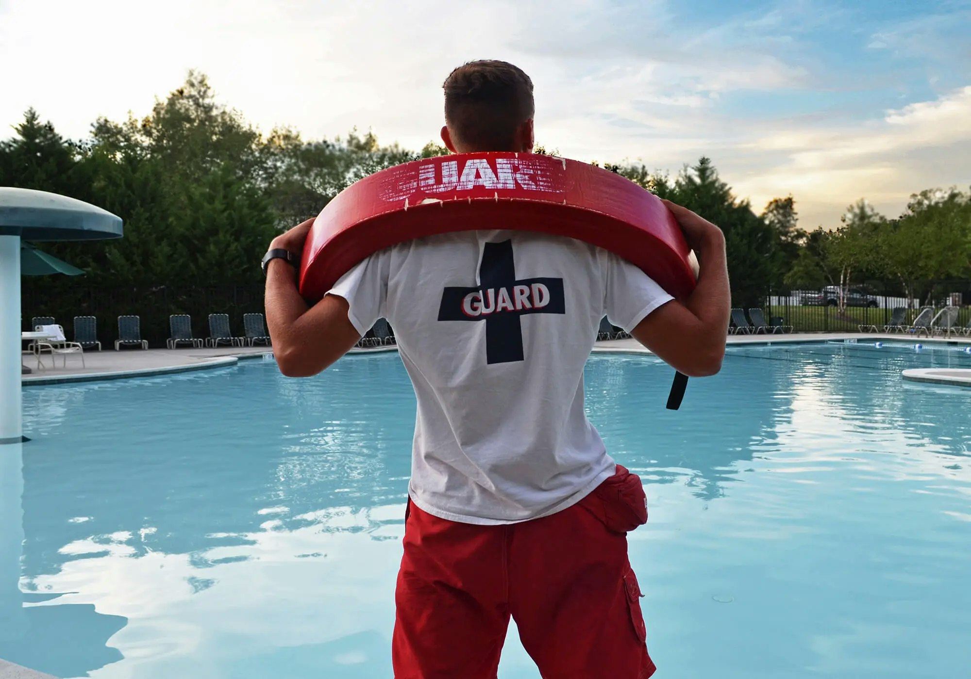 Lifeguard standing by a pool with a rescue buoy, ready to ensure swimmer safety during a tranquil evening.