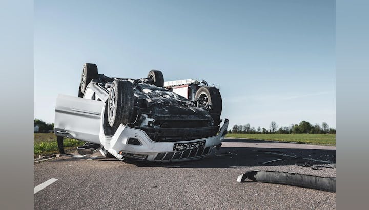 Overturned white car after an accident on a road, debris scattered, no people visible.