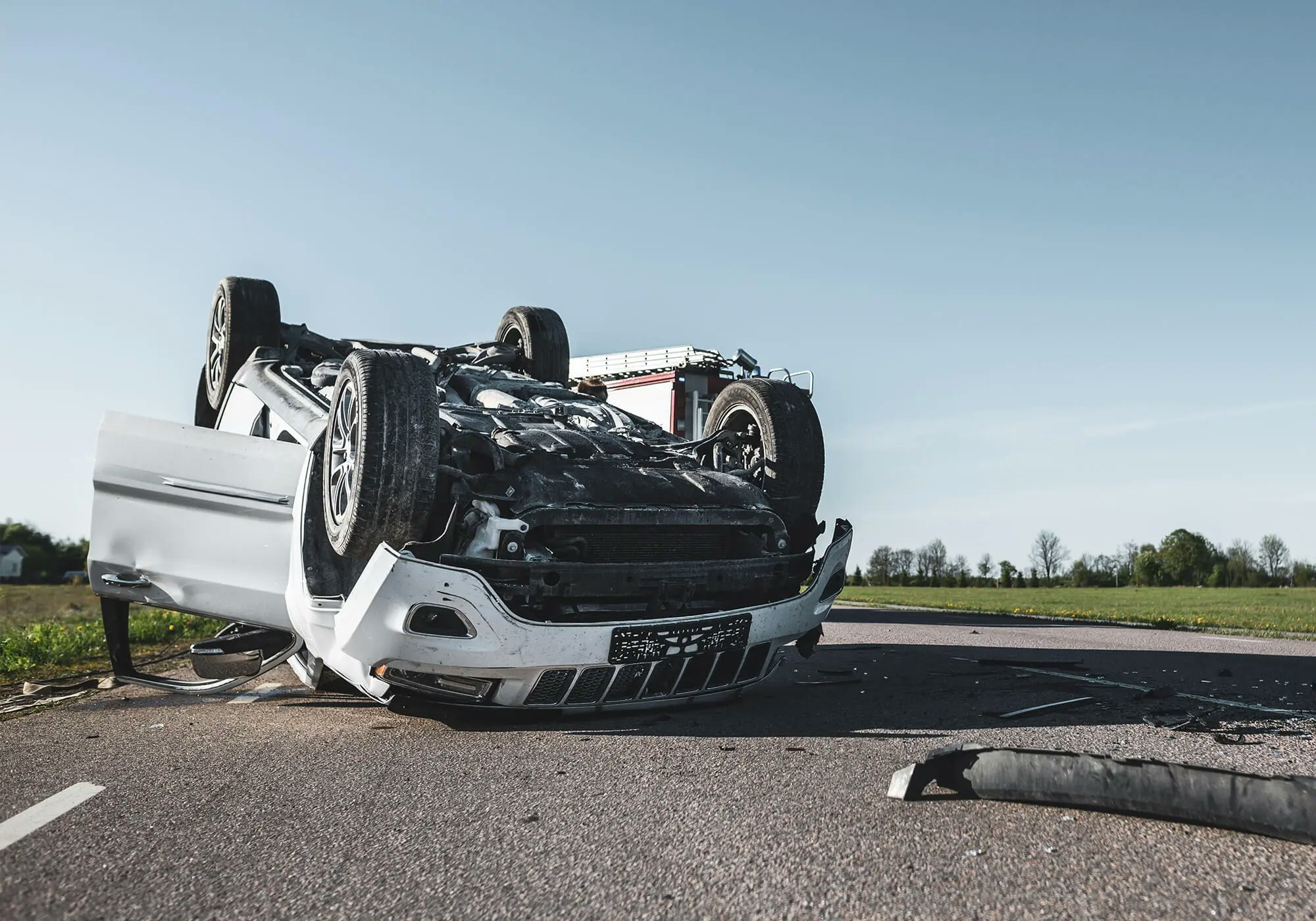 Overturned white car after an accident on a road, debris scattered, no people visible.
