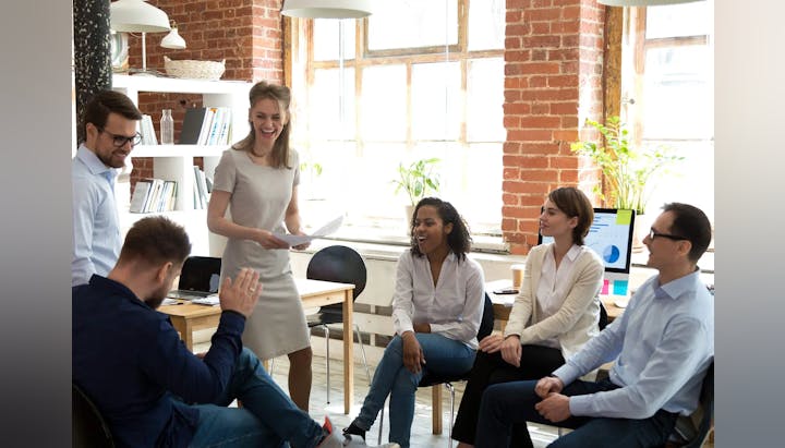 A group of smiling professionals in a bright office space, possibly in a meeting or collaborative session.