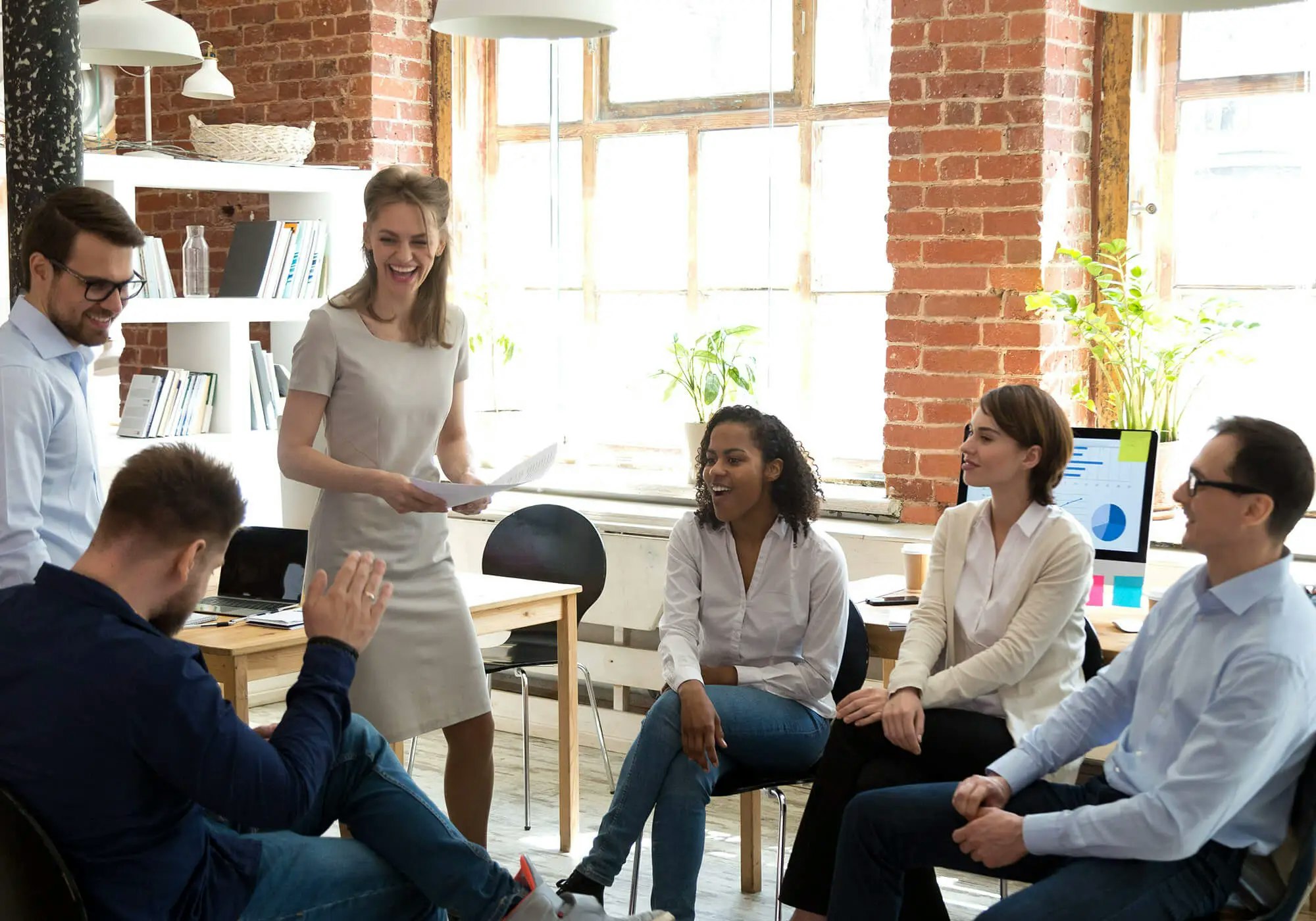 A group of smiling professionals in a bright office space, possibly in a meeting or collaborative session.