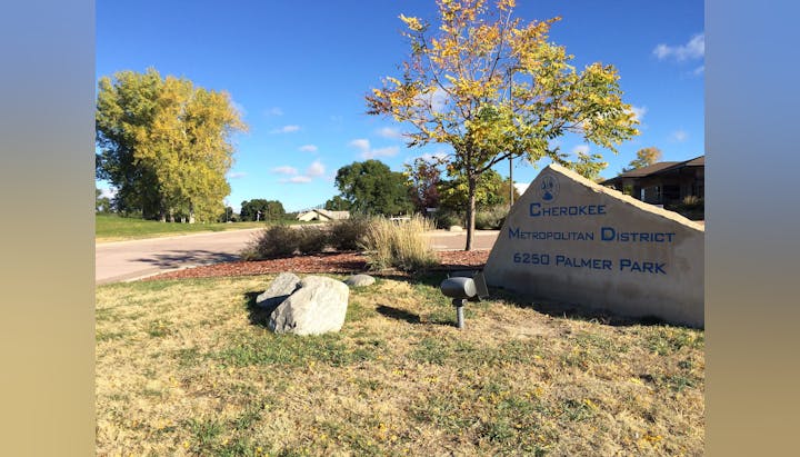 A landscaped area with a sign for "Cherokee Metropolitan District, 6250 Palmer Park", amongst trees and blue sky.