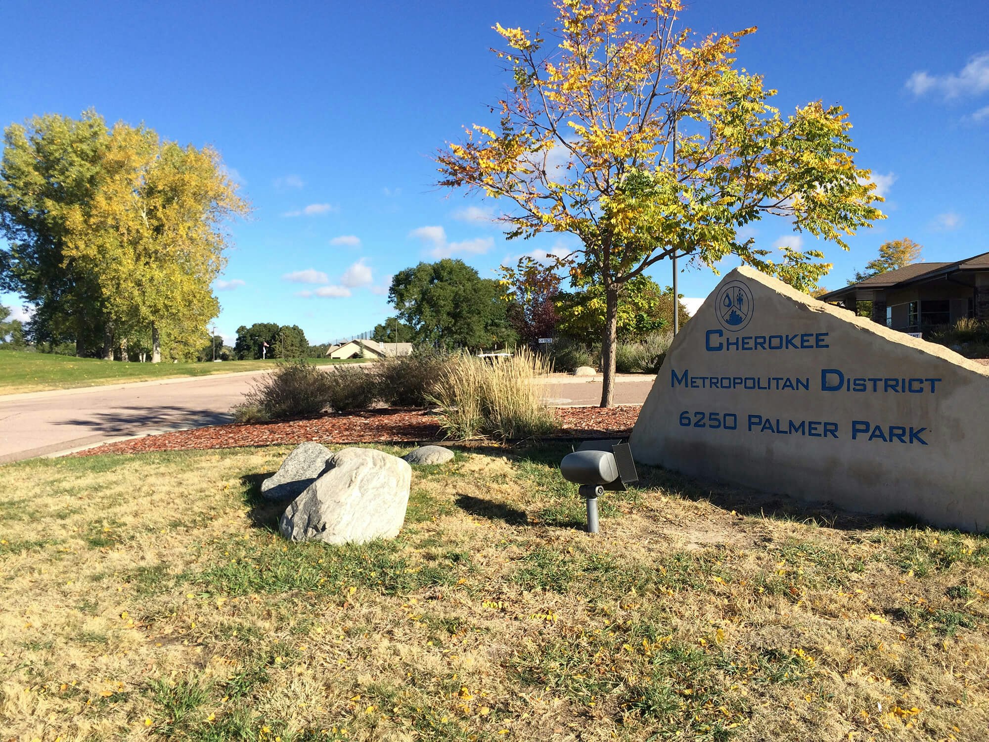 A landscaped area with a sign for "Cherokee Metropolitan District, 6250 Palmer Park", amongst trees and blue sky.