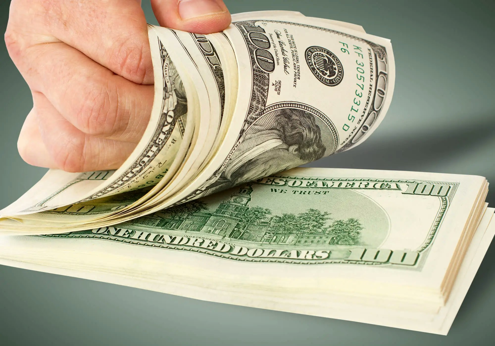 A hand holding a stack of US $100 bills.