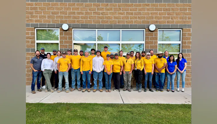 A group photo of a diverse team in yellow shirts standing in front of a building, smiling and posing together.