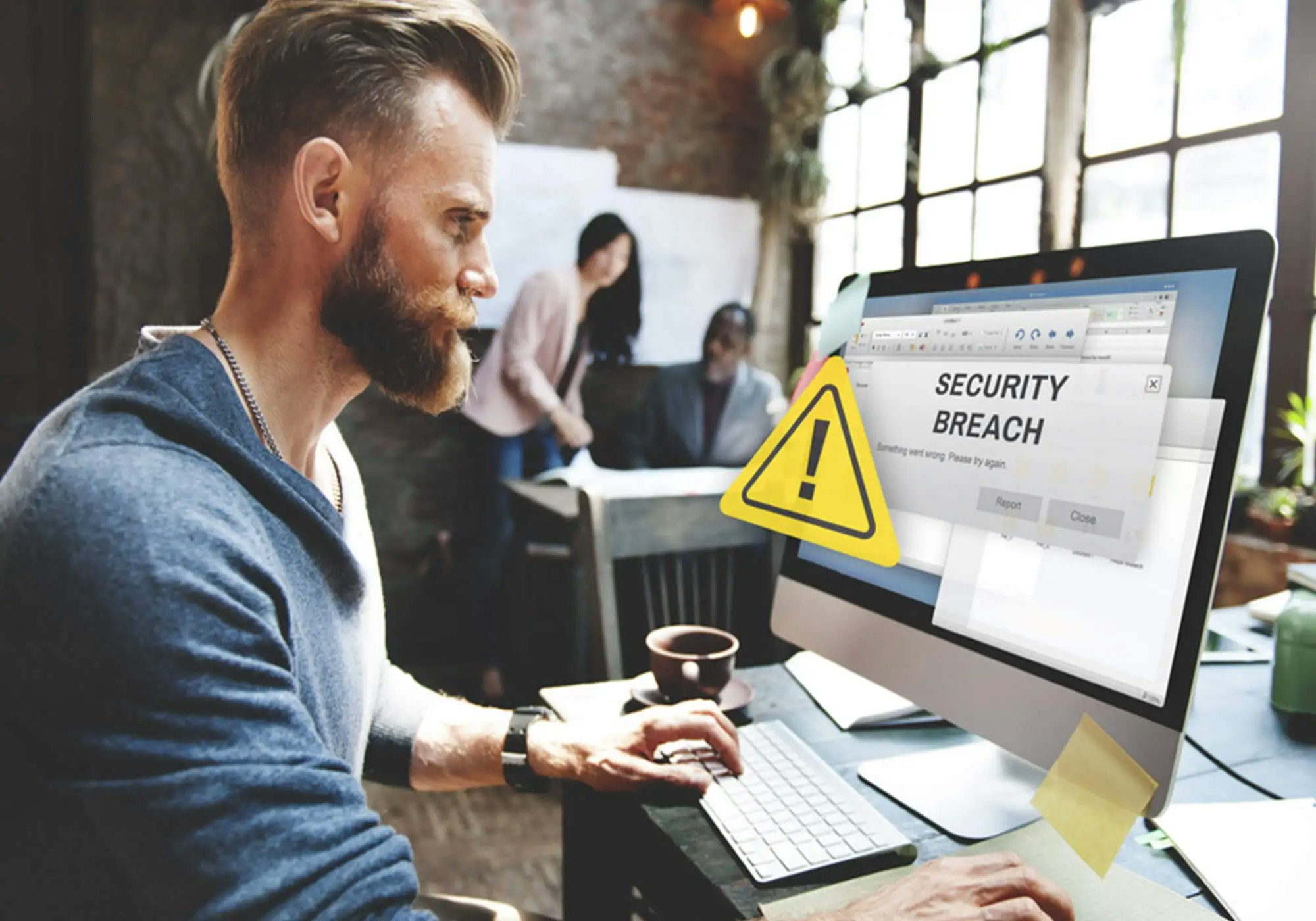 Man at desk with computer displaying a 'Security Breach' warning; colleagues in background.